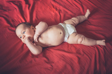 Cute baby in diaper on red bedsheet
