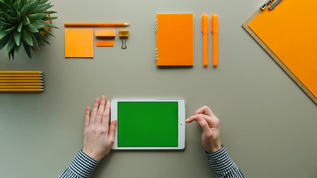 Top view woman using tablet computer with green screen. Orange table background. Chroma key.