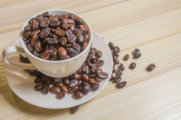 Roasted coffee beans in white cup on wood table