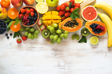 Above view of rainbow colored fruits, strawberries, blueberries, mango, orange, grapefruit, banana, apple, grapes, kiwis on the white background, copy space for text, selective focus