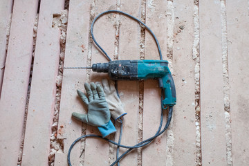 Electric perforator (drill) and working gloves are on the dirty and dusty wooden floor during under...