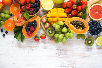 Above view of rainbow colored fruits, strawberries, blueberries, mango, orange, grapefruit, banana, apple, grapes, kiwis on the white background, copy space for text, selective focus