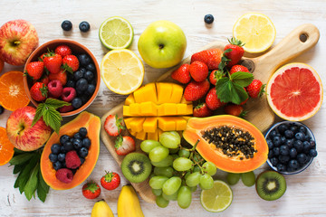 Lots of fruits, strawberries, blueberries, mango, orange, grapefruit, banana, apple, grapes, kiwis on the white background, top view, selective focus