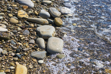 sea pebble beach with multicoloured stones, waves with foam