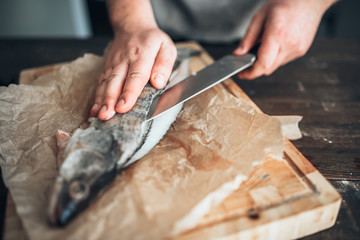 Chef hands with knife cut up fish on cutting board - obrazy, fototapety, plakaty