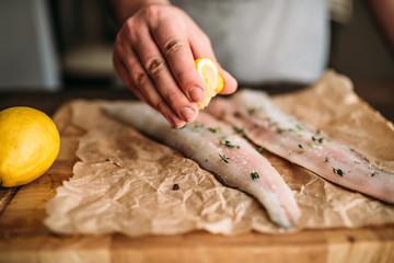 Chef hands squeeze lemon on raw fish closeup view
