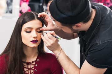 Male make-up artist Paints eyelids to brunette girl in beauty salon, close up