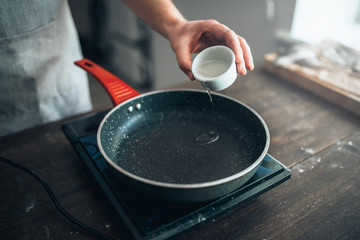 Male person hands pour oil in a frying pan