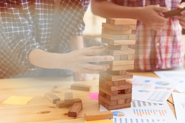 young start up people take one block from wooden blocks tower with marketing and financial graph and chart on table, planning, risk and strategy in business