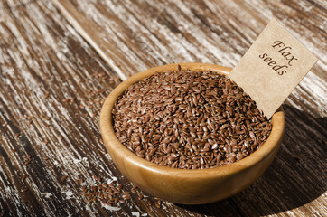 Close up of brown flax seeds  in wooden bowl with tag on a rustic table. Superfood: linseeds are high in omega-3 fatty acids, essential for good health. Healthy eating ,vegan diet concept.