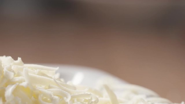 Slow motion slide shot of grated pizza mozzarella cheese falls in plate, 180fps prores footage