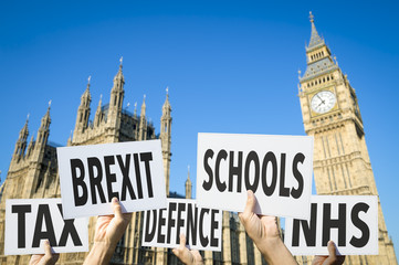 Hands holding signs protesting modern British social issues like Brexit, tax, education, defense,...