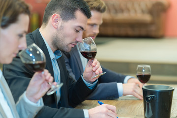 three people smelling and evaluating red wine in wineglasses