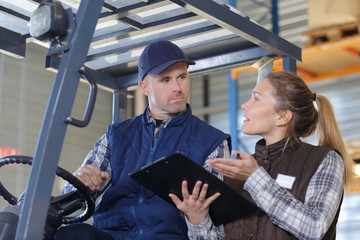 fork lift truck driver discussing checklist with manager in warehouse