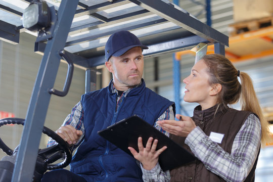 fork lift truck driver discussing checklist with manager in warehouse