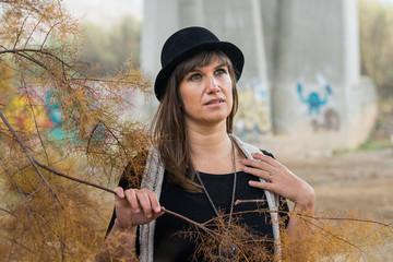 Mujer joven con sombrero junto al puente de cemento