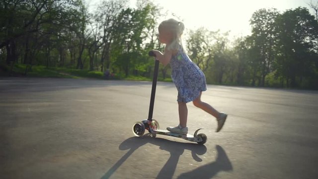 Beautiful little girl pushes herself on her scooter slow motion