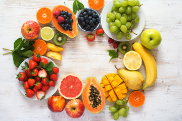 Rainbow color fruits arranged in a circle, strawberries, blueberries, mango, orange, grapefruit, banana, apple, grapes, kiwis on the white background, copy space for text, selective focus