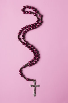 Rosary on a pink background. Christian cross.