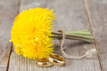 Fototapeta na wymiar Wedding rings and bunch of yellow dandelion flowers