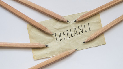 Word 'Freelance' on a piece of brown paper with pencils on white background