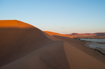 Fototapeta na wymiar Climbing Big Daddy Dune during Sunrise with View onto Salt Pan and Desert Landscape, Sossusvlei, Namibia