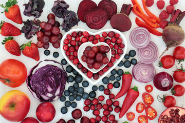 Purple and red health food with fresh fruit and vegetables in heart shaped porcelain dishes and loose on distressed wood background. High in antioxidants, vitamins, anthocyanins and dietary fibre.