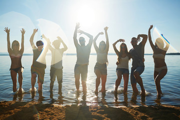 Obraz premium Energetic friends dancing in water by sandy beach