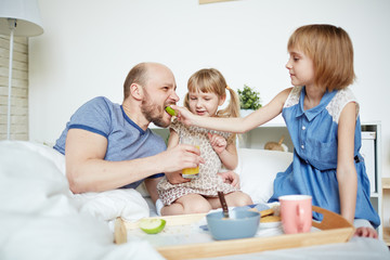 Youthful daughters feeding their father in the morning