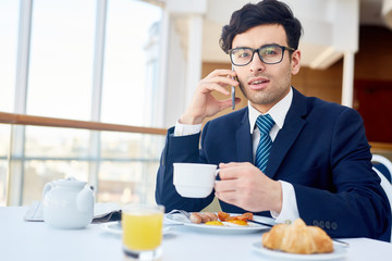 Mobile businessman with drink looking at camera by breakfast