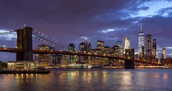 Time-lapse of Lower Manhattan Financial District skyscrapers, Brooklyn Bridge, and East River with passing clouds at twilight. Manhattan, New York City