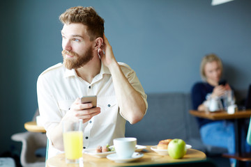 Pensive businessman with smartphone sitting in cafe