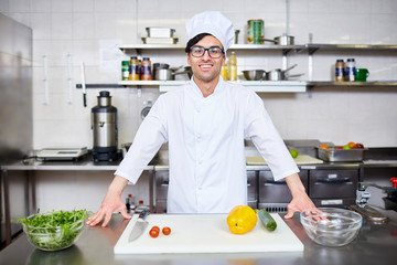 Young chef in uniform standing by his workplace