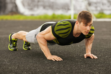 Fitness man doing push-ups in the stadium, cross training workout. Sporty male training outside