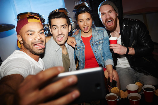 Group of modern young people chilling at night club party, posing for selfie photo, grimacing and having fun