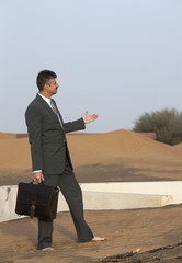 businessman with a briefcase in  a desert village, pointing at a old house in a sand