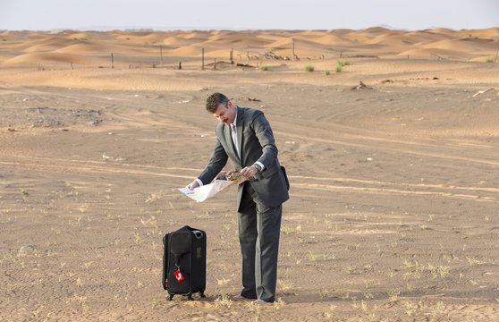 businessman in  a desert with a suitcase, looking at a map
