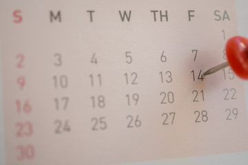 Calendar page with a written heart thumbtack on date of February 14 Valentine's day.