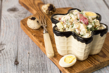 Salad.   Freshly prepared salad in a figured ceramic salad bowl, quail eggs and fork on a cutting board on a gray wooden background.