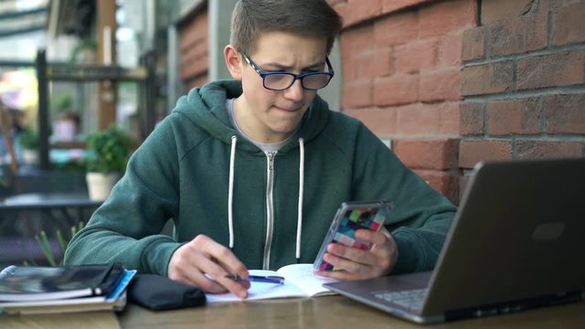 Boy with smartphone and notepad doing homework by table in cafe
