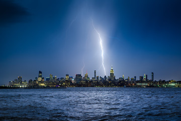 Fototapeta premium Lightning striking New York City skyscrapers at night. Stormy skies over Midtown Manhattan from the Hudson River