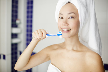 Portrait of smiling Asian woman brushing white teeth in shower during beauty treatment routine and looking at camera