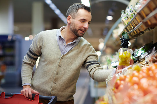 Portrait of smiling handsome man grocery shopping in supermarket, choosing food products from shelf