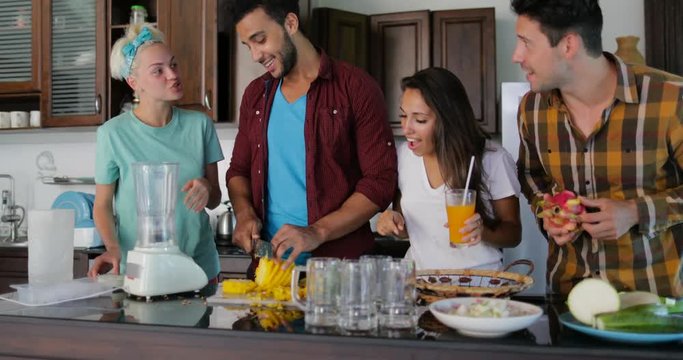 Two Couples In Kitchen Cooking Together, Young Man Chopping Pineapple People Group Talking Cut Vegetables And Fruits Prepare Healthy Meal Slow Motion 60