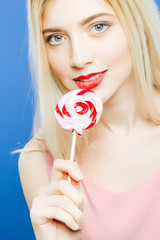 Sexy Young Blonde with Sensual Lips and Colorful Lollipop in Hands Looks at the Camera on Blue Background in Studio.