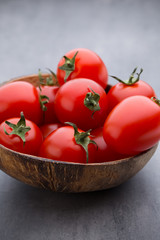 Small plum tomatoes in a wooden bowl on a gray background.