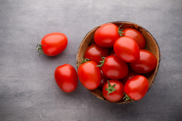 Small plum tomatoes in a wooden bowl on a gray background.