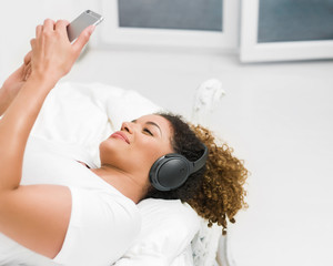 Woman relaxing on bed while listening to music and looking at smartphone