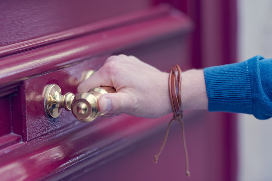 Hand holding a door knob on the red wooden door