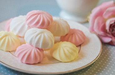 Delicate multi-colored marshmallows on white openwork plate. Still life with marshmallows, a Cup of tea and a pink rose on vintage background.